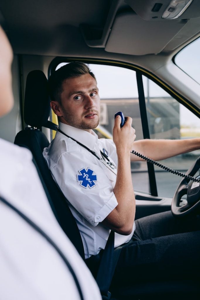 A paramedic in uniform communicates using a radio while seated inside an ambulance.